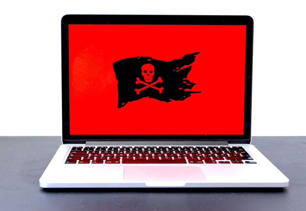 Laptop on benchtop with red background on screen with black flag displaying skull and crossbones.jpeg